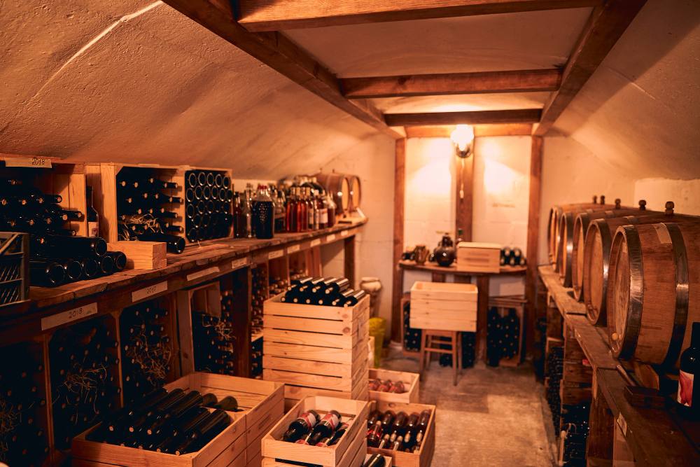 Cave à vin avec bouteilles de boissons alcoolisées dans des caisses en bois et des tonneaux sur des supports en bois